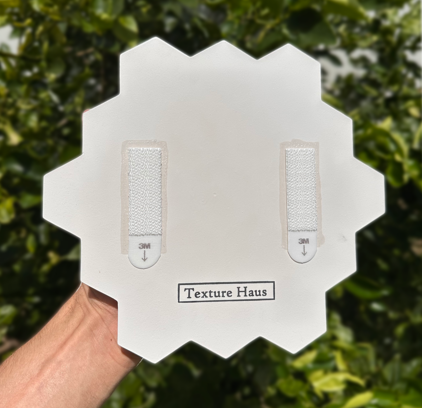 Hexagonal tool with textured surfaces held by a hand against a green leafy background, branded 'Texture Haus'.