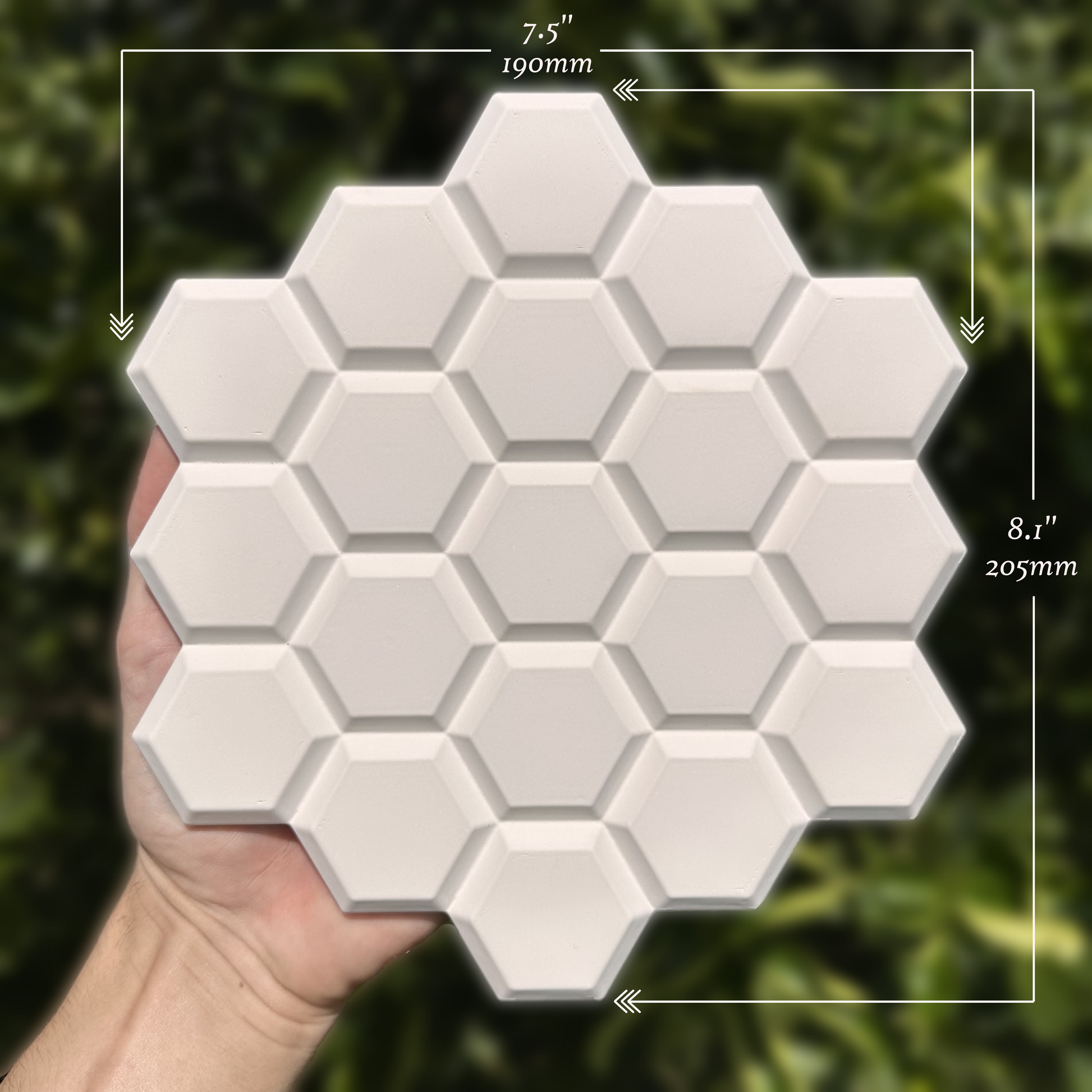 Hexagonal white tiles held by a hand with measurements overlaid on a blurred green background